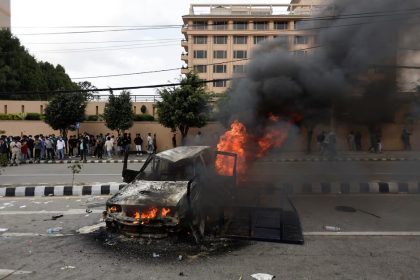 Orang-orang berdiri di dekat sebuah kendaraan yang dibakar oleh para demonstran saat aksi protes menentang korupsi dan keputusan pemerintah memblokir sejumlah platform media sosial, di Kathmandu, Nepal, 8 September. Sumber foto : REUTERS